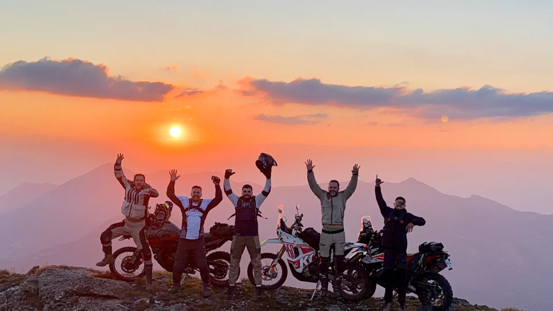 Six riders celebrating together on a ridge at sunset