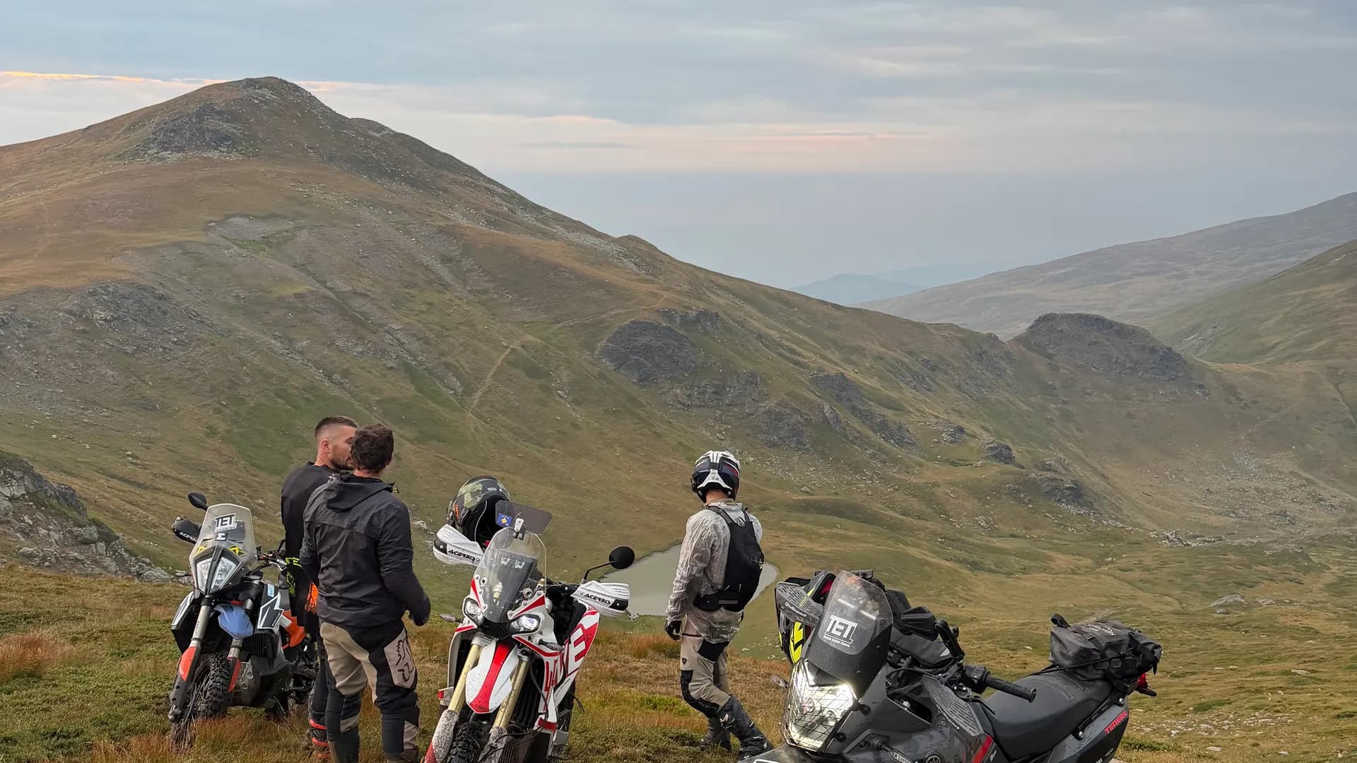 Riders and bikes strung along a high grassy ridge in soft light