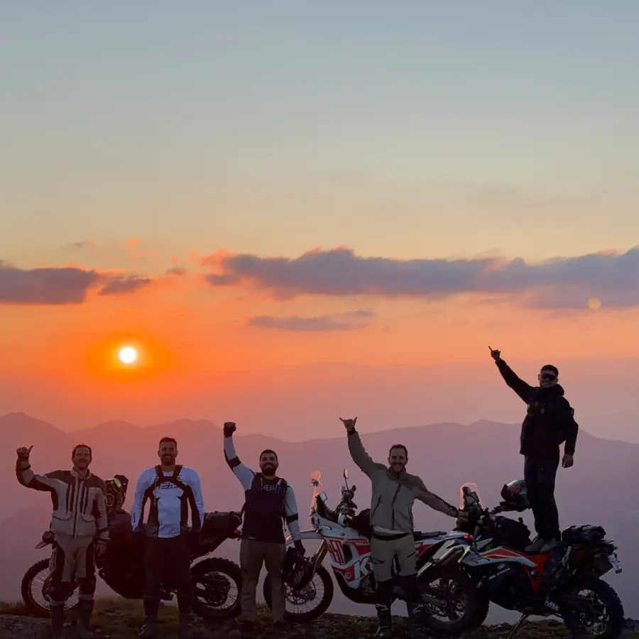 Riders celebrating on a summit at sunset