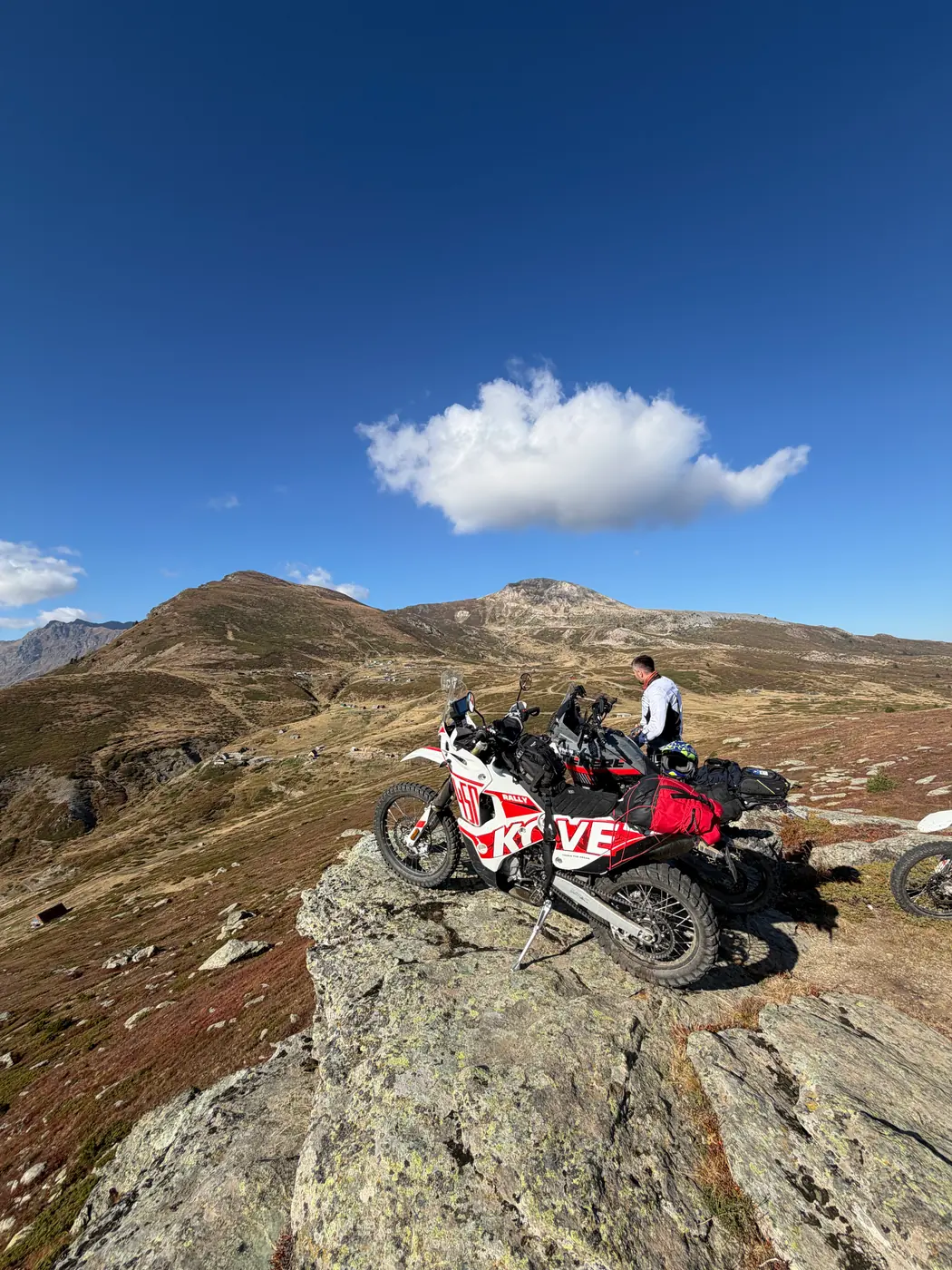 Two rally bikes parked on a rocky outcrop, open high moorland and rounded summits behind, in the Accursed Mountains, northern Albania