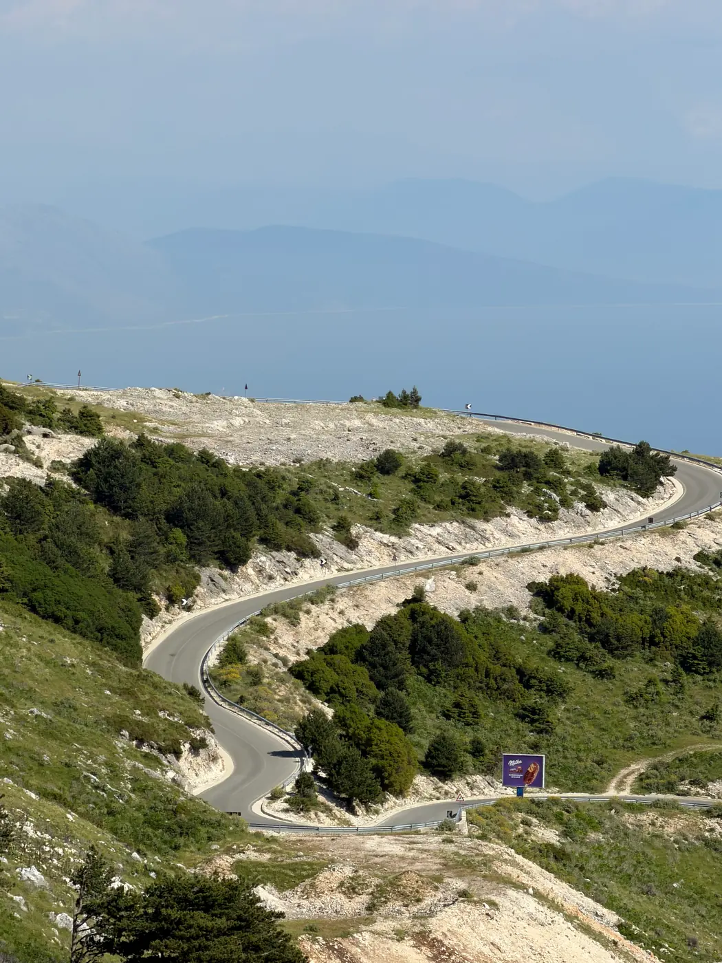 A road winding along a headland high above the Ionian Sea in southern Albania, a hazy peninsula on the horizon